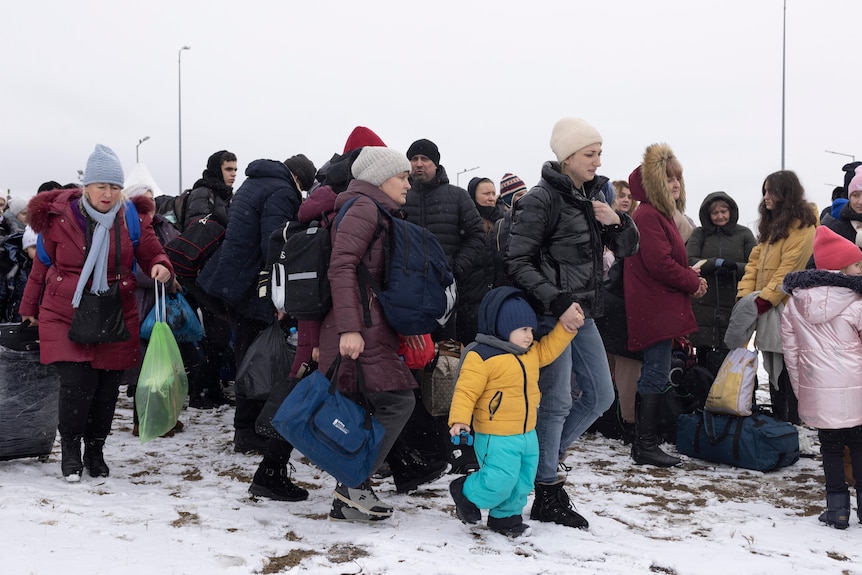 A group of women and children in winter clothing walk through the snow.