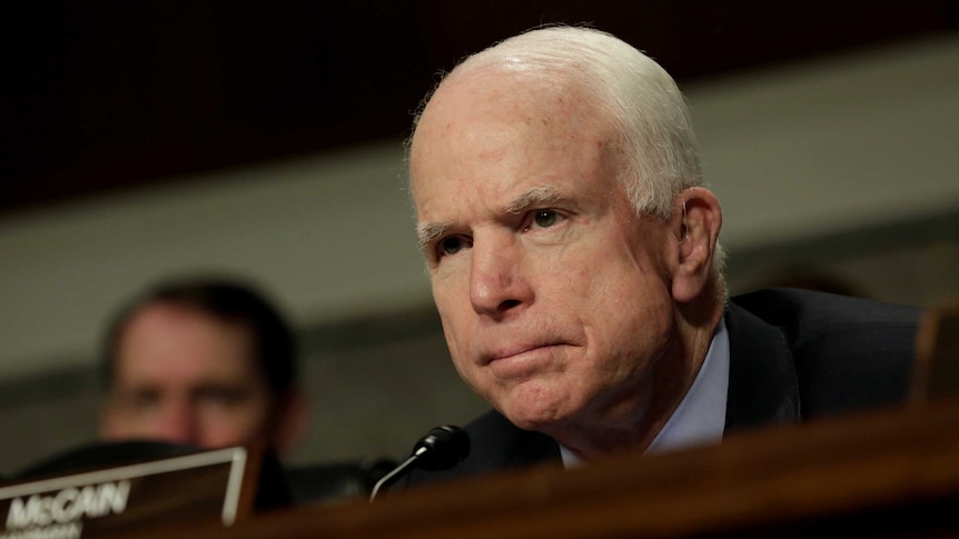 Senator John McCain looks stern as he looks into the distance at a committee hearing.
