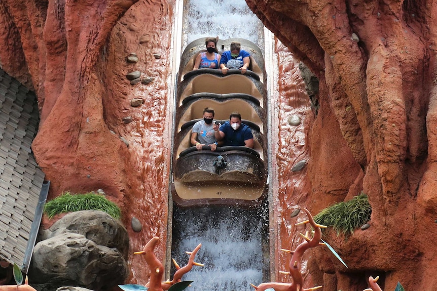 People wear masks and leave empty seats in between themselves on a ride at Disney World.