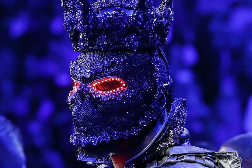 Deontay Wilder wears a large, black, spiked helmet which is covered in sequins and lights. He has a skull on his shoulder.