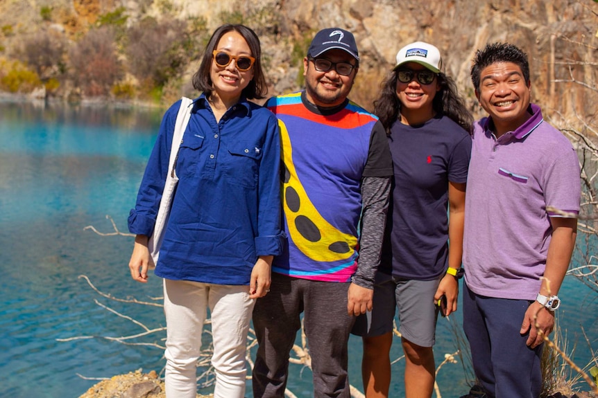 Four tourists stand in front of bright blue water in the mine pit of Mary Kathleen.