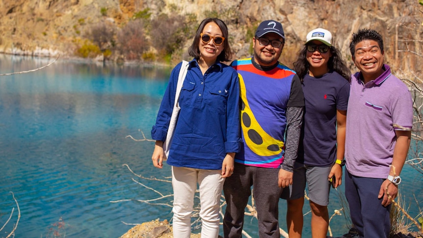 Four tourists stand in front of bright blue water in the mine pit of Mary Kathleen.