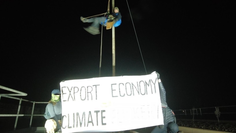 Two people atop a rail bridge protesting coal, holding a sign 