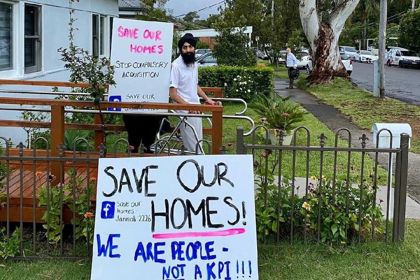 A man with a beard next to a save our homes sign on a ramp in a suburban street