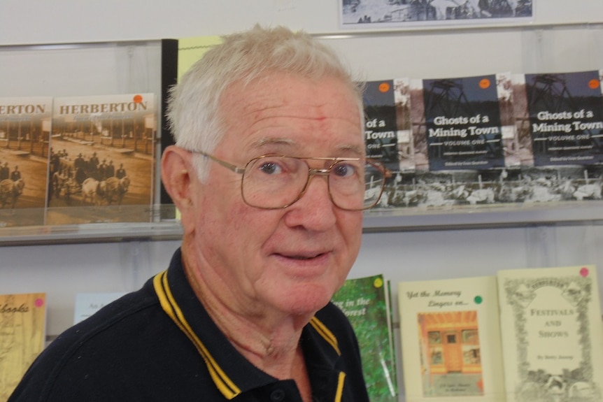 Profile photo of Ivan Searston smiling with historical books about his town of Herberton behind him.