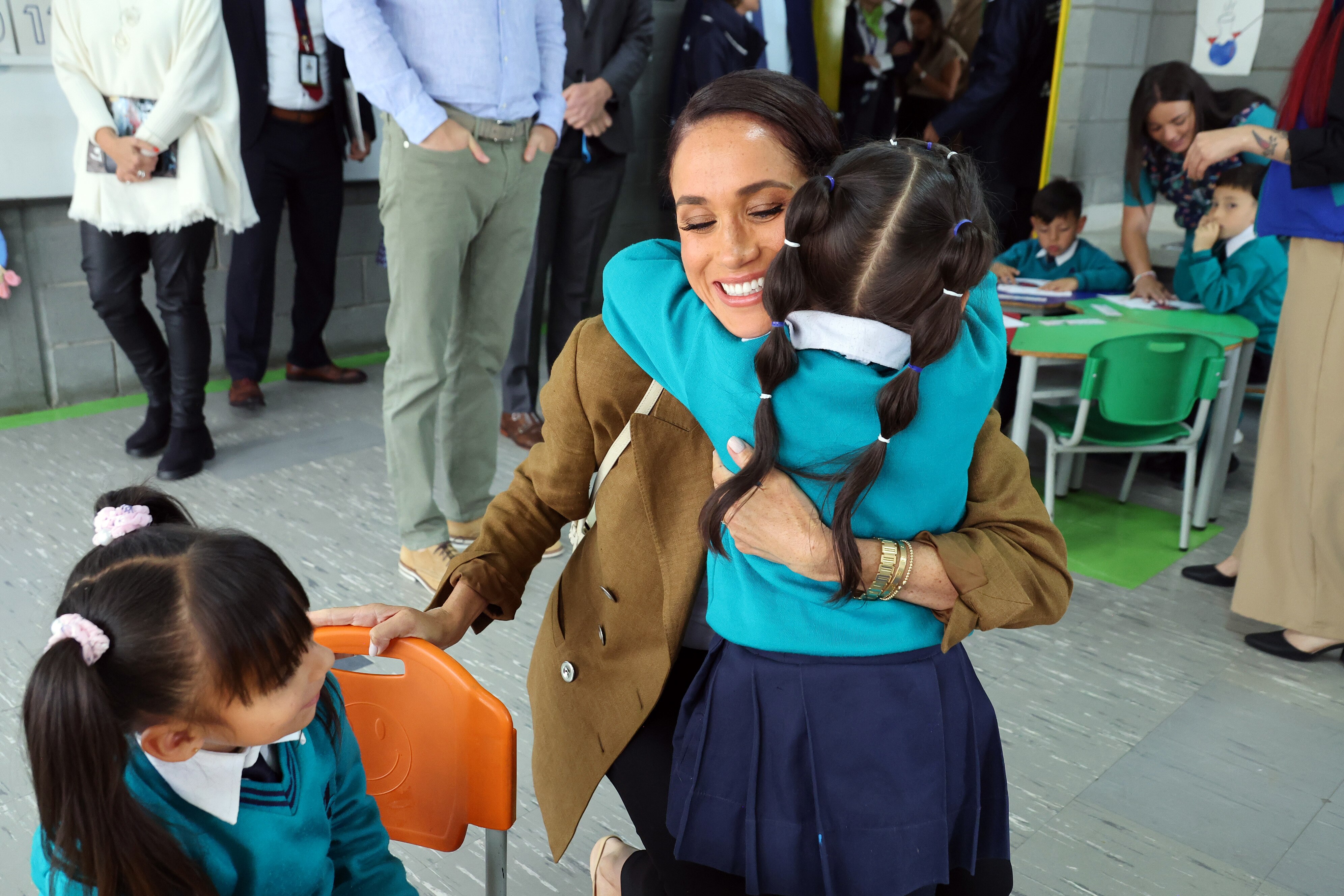 Meghan smiles as she crouches down and hugs a schoolgirl.
