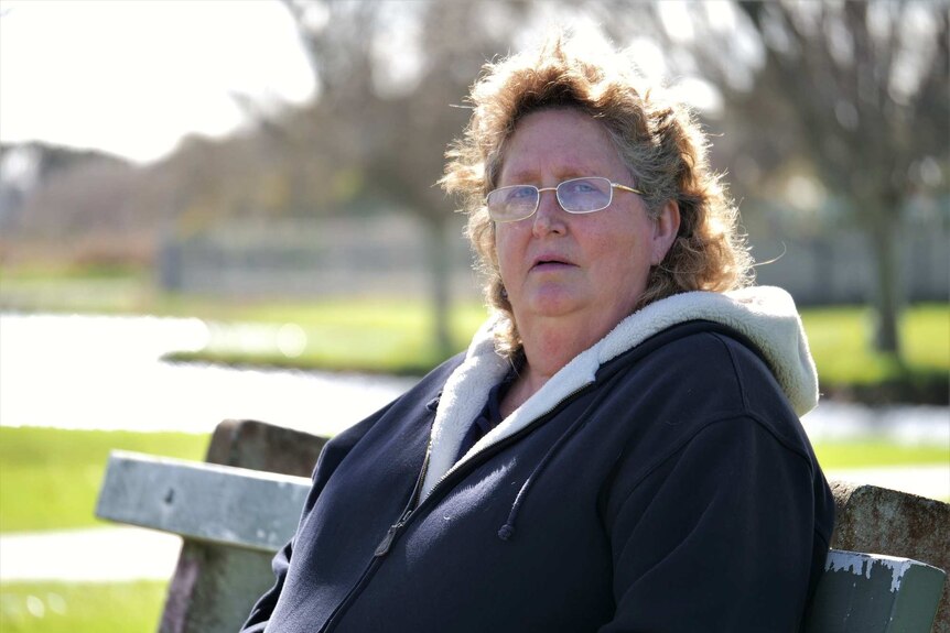 A woman sitting on a park bench with an anguished expression.