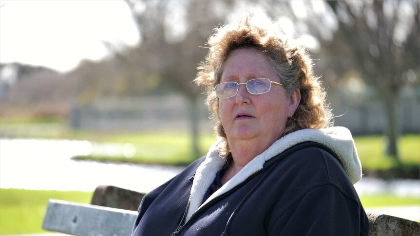 A woman sitting on a park bench with an anguished expression.