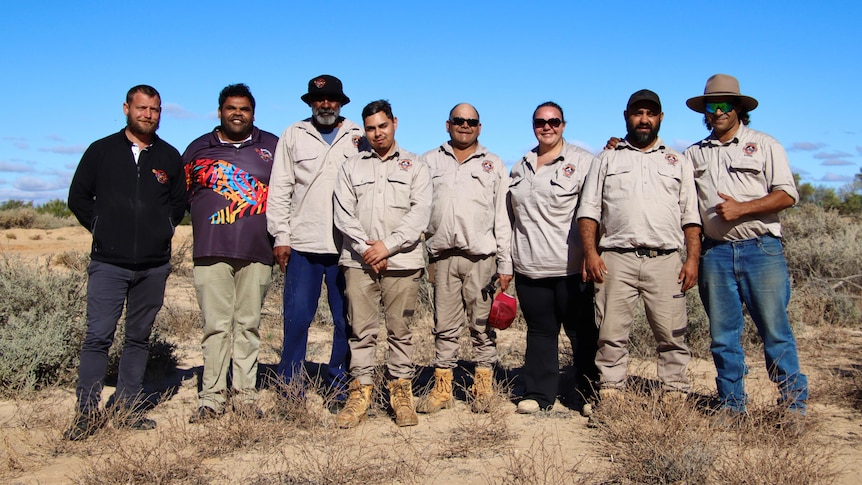 A row of indigenous men and women stand in a line smiling in a national park