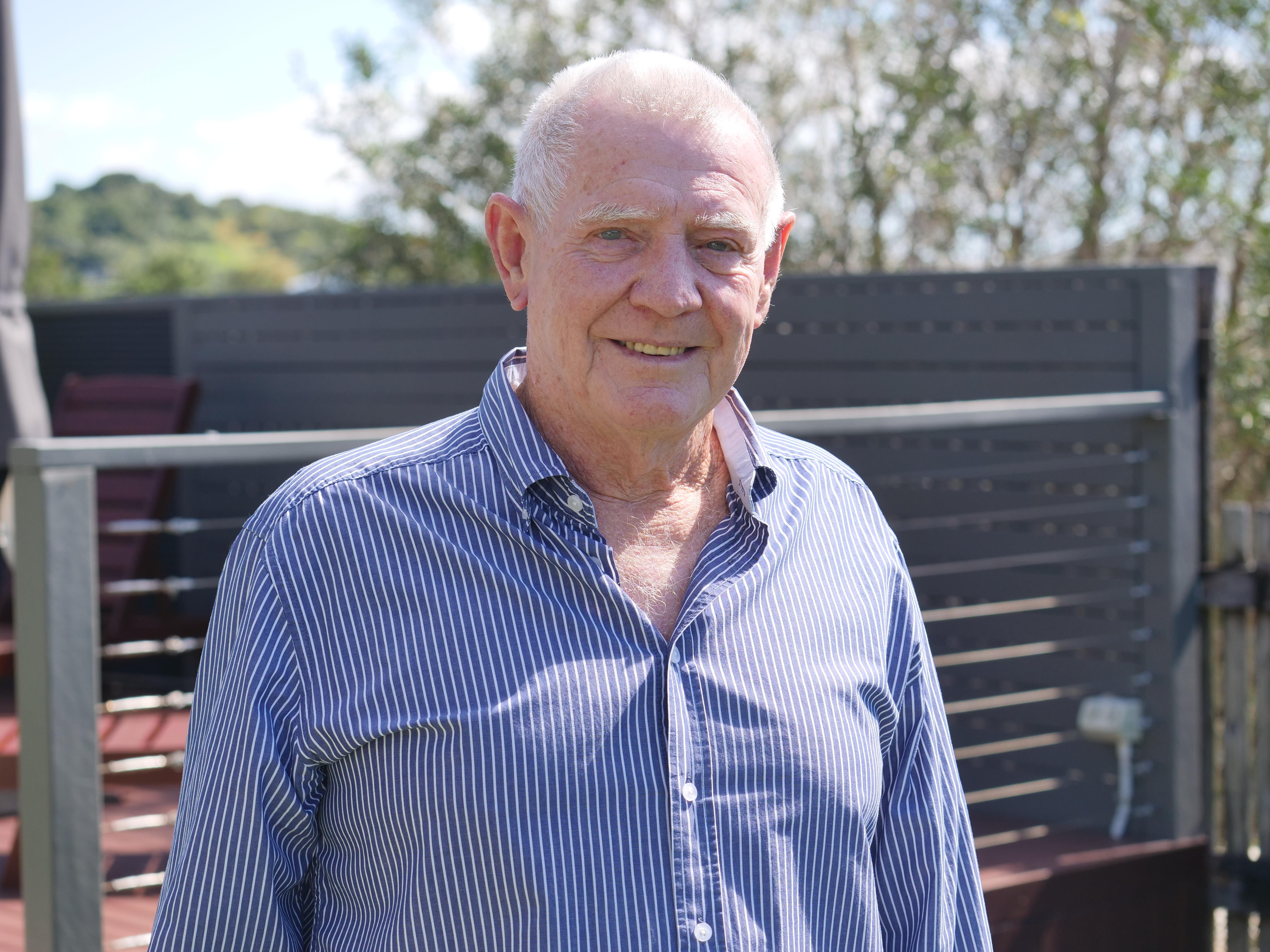 An older man in a backyard smiling at the camera