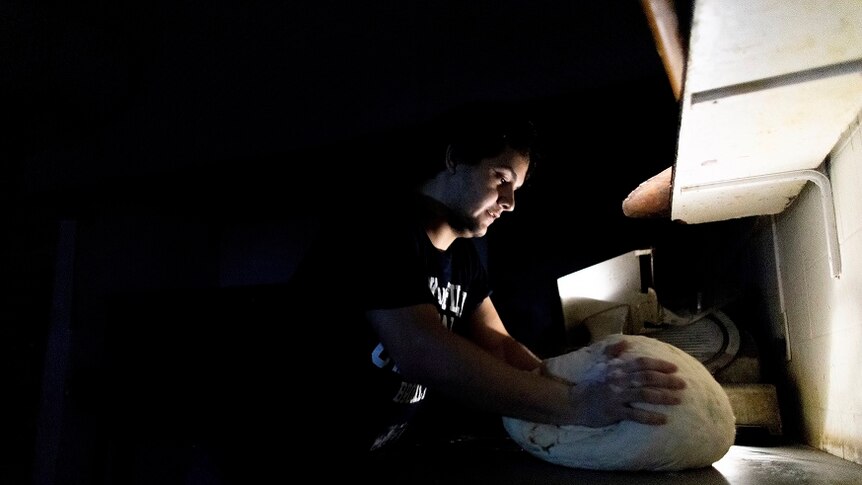 A pizza maker uses battery-powered lamps to illuminate his work space during a blackout.
