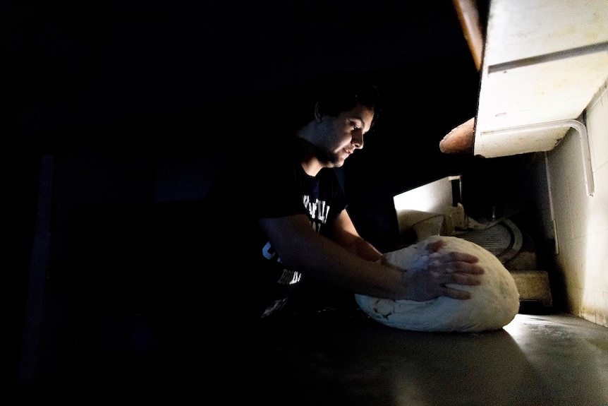 A pizza maker uses battery-powered lamps to illuminate his work space during a blackout.