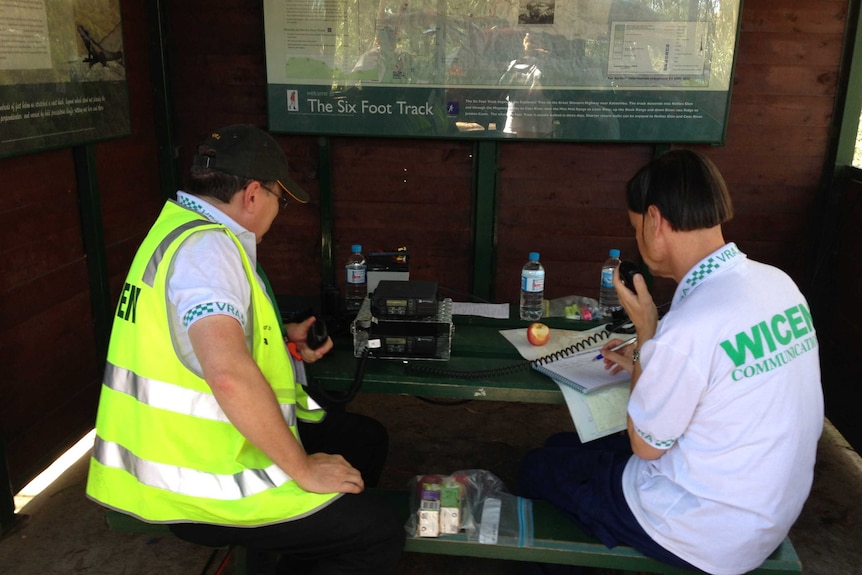 Two people using two-way radios in a hut with maps of the Six Foot Track.