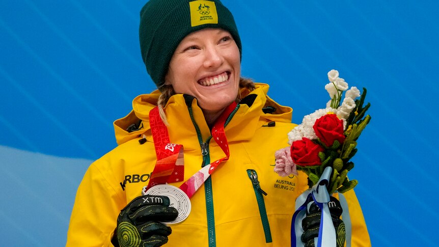A woman in green and gold smiles holding a silver medal.
