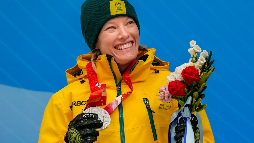 A woman in green and gold smiles holding a silver medal.