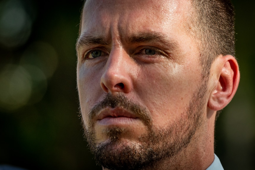 a close up shot of a man's face staring to the distance. He has short mousy brown hair and a short beard.