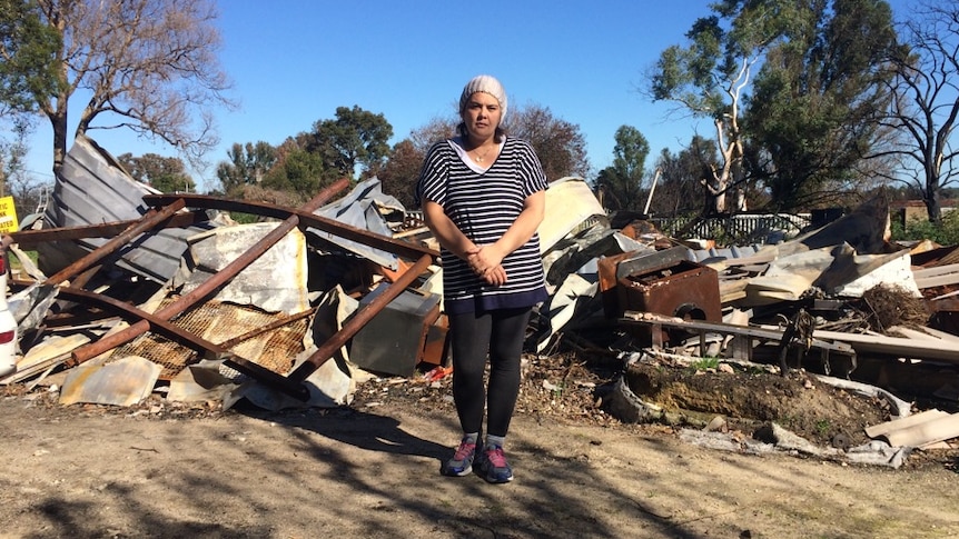 Woman stands in front of burnt house