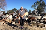 Woman stands in front of burnt house