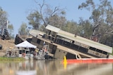 An historic paddle wheeler emerges from the brown water of the Thomson River, with salvage crews on pontoons and machinery.