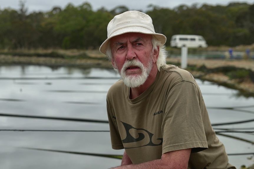 John Luckens frowns and looks off to the side while squatting down next to one of his marron ponds