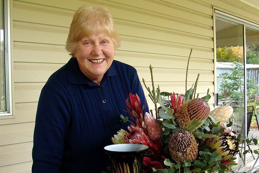 Women smiles while holding a bunch of Australian native flowers.
