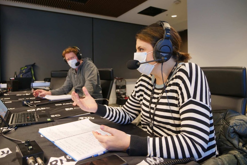 A woman with a mask and headset on talks animatedly, while a man with a mask and headset listens