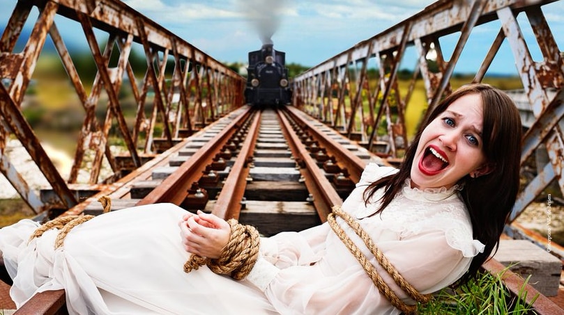 A woman wearing a white dress screams while tied to train tracks with her hands bound as high speed train approaches.