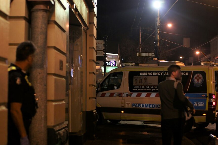 An ambulance arrives at a Melbourne CBD hotel at night. A police officer stands nearby.
