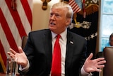 US President Donald Trump gestures with his hands while sitting in front of a US flag.