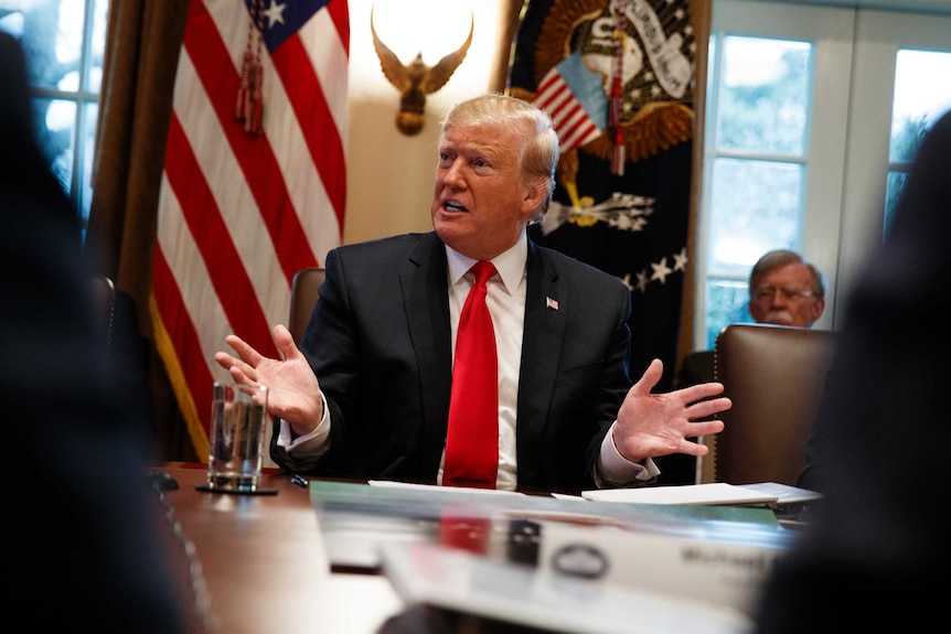 US President Donald Trump gestures with his hands while sitting in front of a US flag.