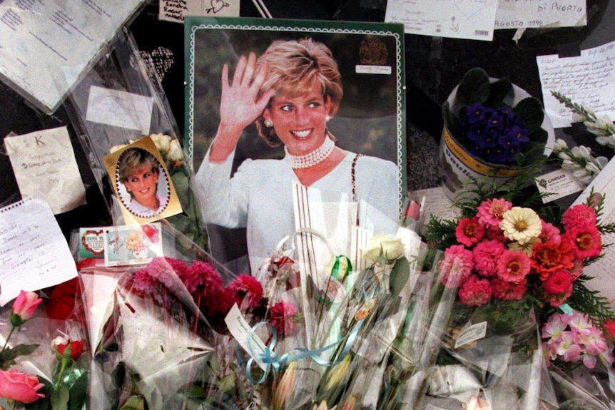 Flowers, photographs, candles and cards are piled up around a photo of Princess Diana.