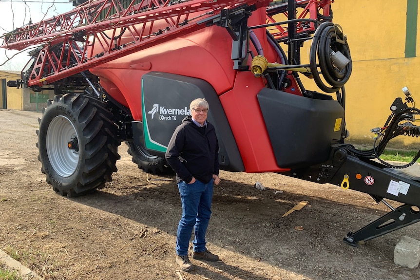 a man stands in front of a large red harvest machine