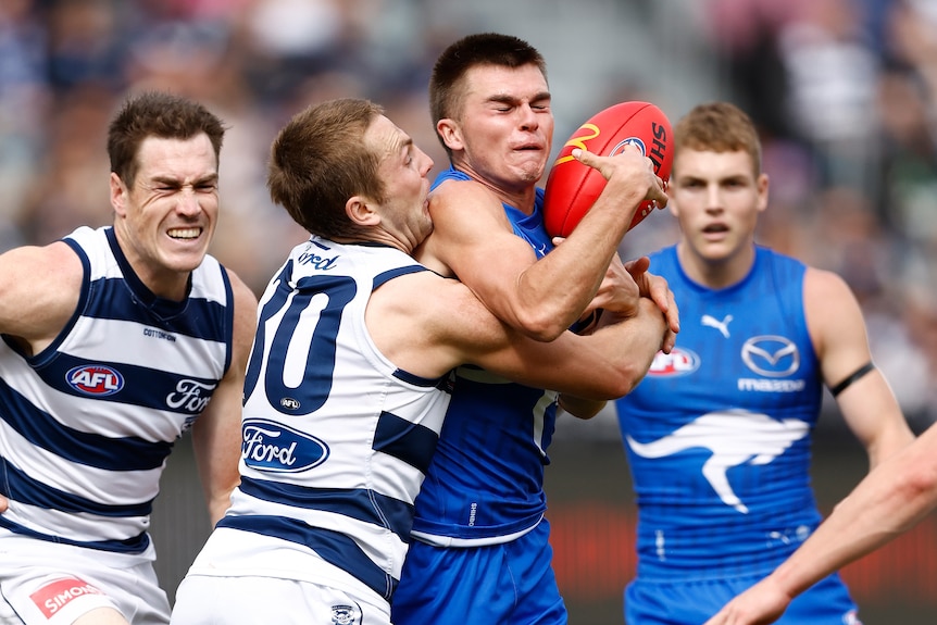 Colby McKercher of the Kangaroos is tackled by Tom Atkins of the Cats, with other players converging