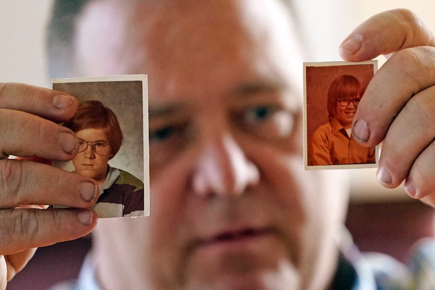 A man holds up two photos of himself as a young boy.