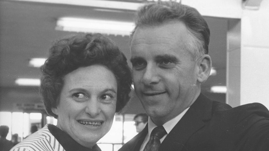 Black-and-white photo of a man and a woman smiling at the airport.