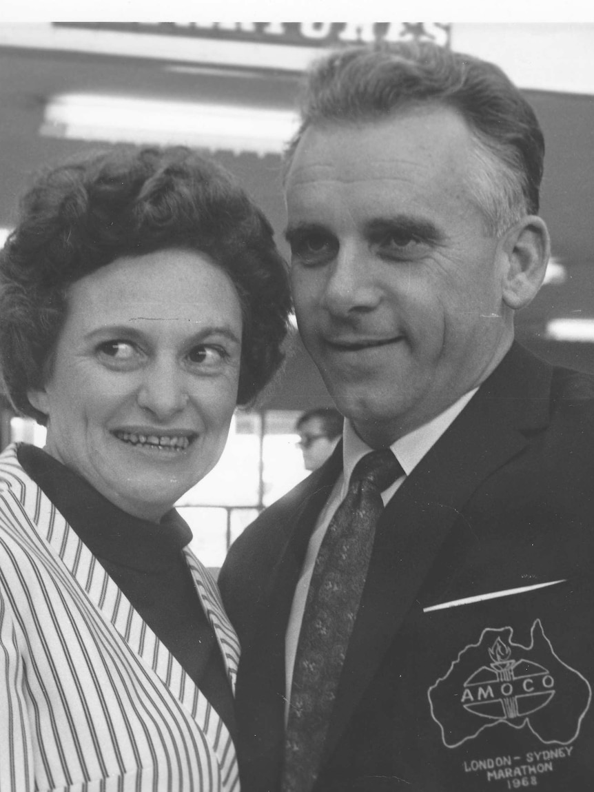 Black-and-white photo of a man and a woman smiling at the airport.