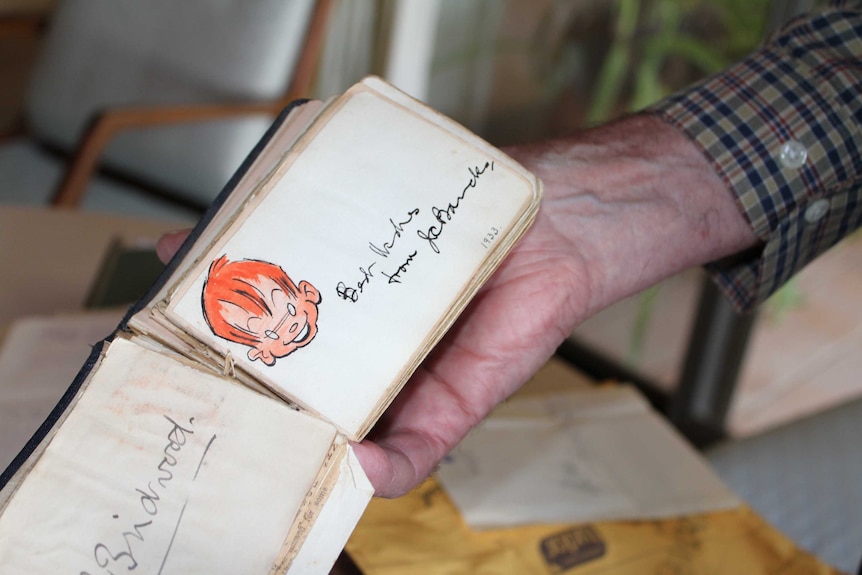 An old autograph book open to a page showing a signature and sketch of the cartoon character Ginger Meggs.