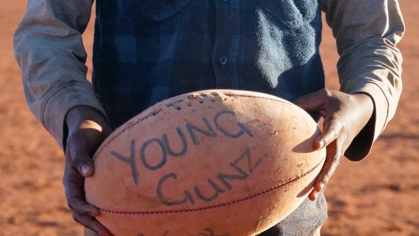 A young boys holds a football with 'Young Gunz' written on it