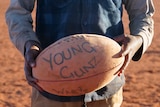A young boys holds a football with 'Young Gunz' written on it