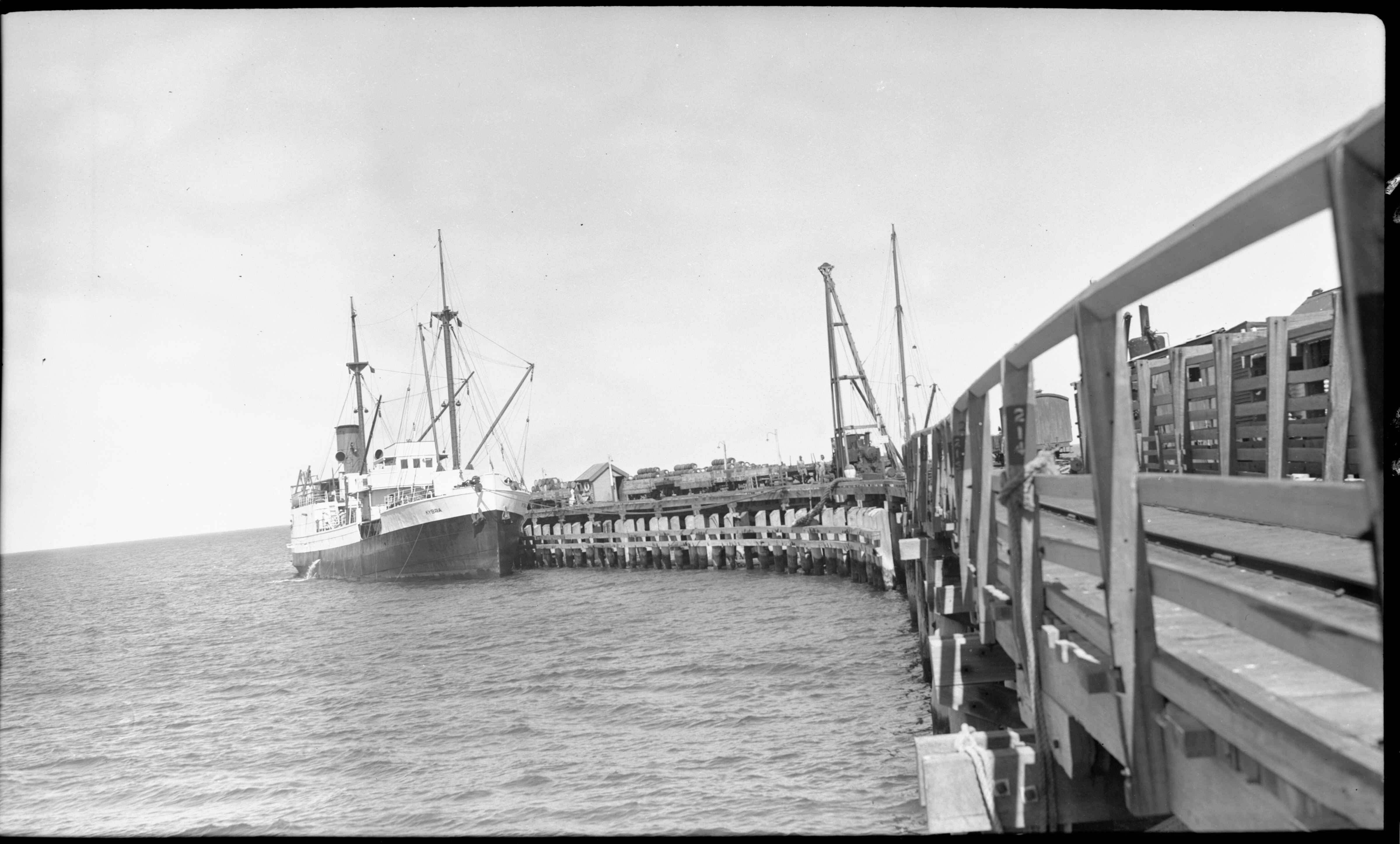 A black and white photo of a fishing boat at the end of a long jetty.
