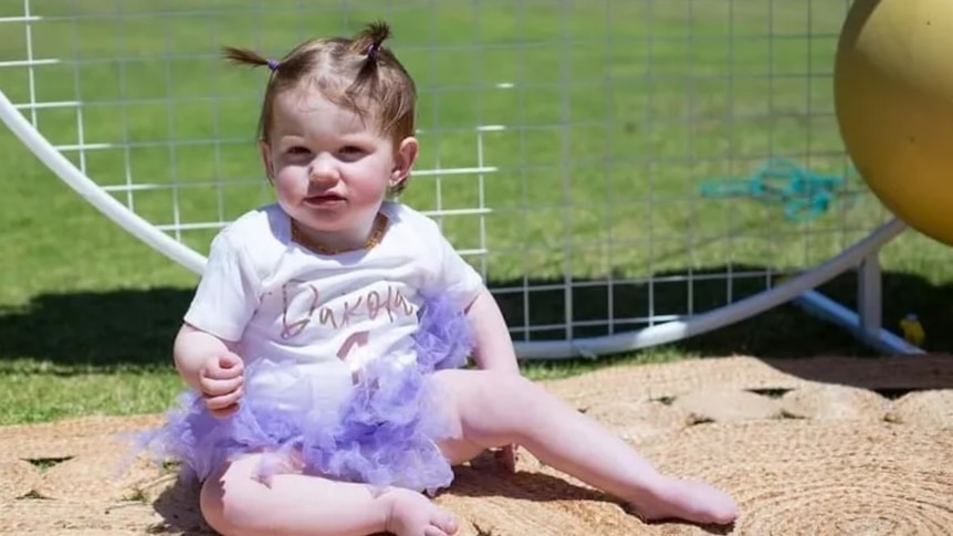 A toddler sits in sand.