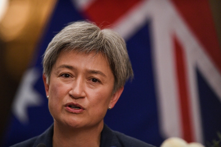 A close up of Penny Wong, a Malaysian Australian woman with short greying hair, with Australian flag in the background.