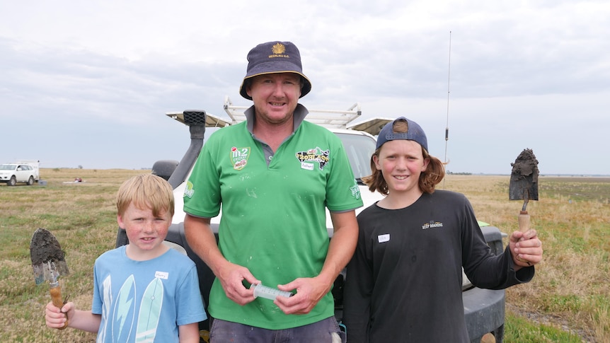 A man and his two sons lean against a ute, holding trowels. 