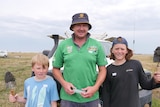 A man and his two sons lean against a ute, holding trowels. 