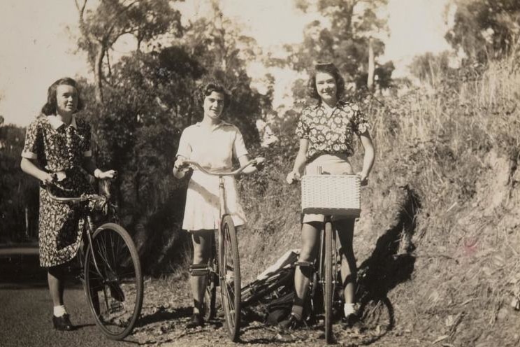 Sepia-toned image of three young women on bikes.