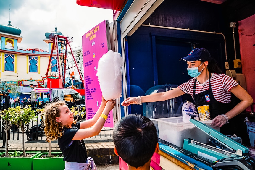 A woman hands a stick of fairy floss to a child at Luna Park.