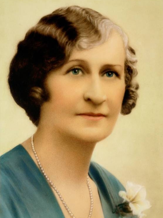 An old photograph of a woman with brown hair wearing a pearl necklace and blue dress.