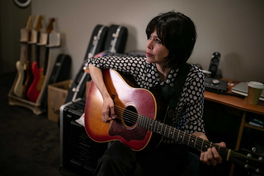 A woman with short hair on guitar looking away from the camera