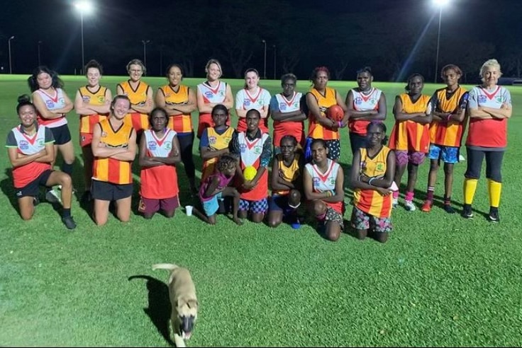 Women's AFL team team pose for photo on football field with puppy at front