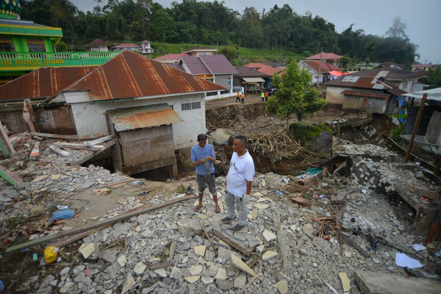 Men stand near a damaged house in an area affected by heavy rain and flash floods.
